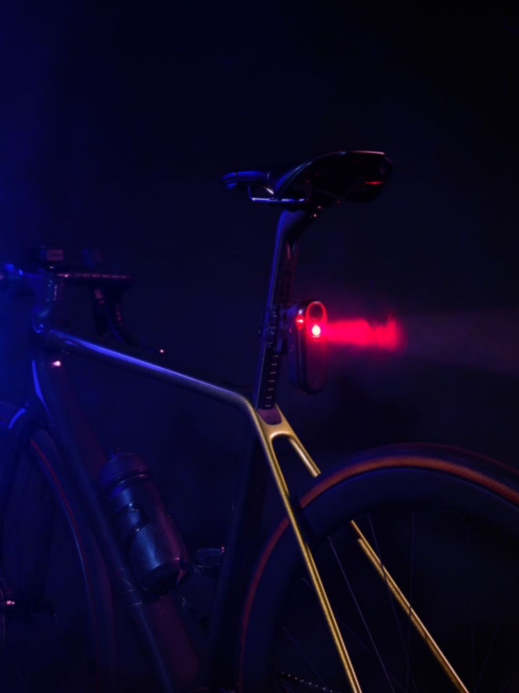 The rear light of a road bike beams through light mist.